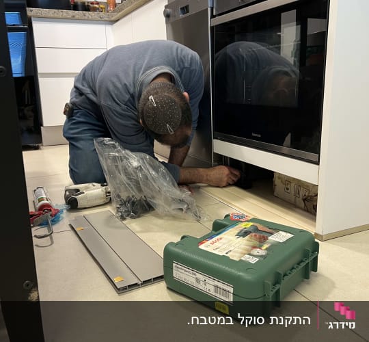 בעל מקצוע במהלך התקנת צוקל מתחת לארונות מטבח ותנור בנוי